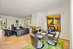 Uma sala de estar moderna com lareira, área de jantar com mesa redonda e um grande quadro abstrato na parede.
