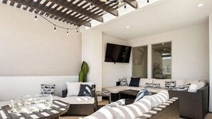 Un espace extérieur moderne, aménagé avec un canapé, une table ronde et un téléviseur fixé au mur.
