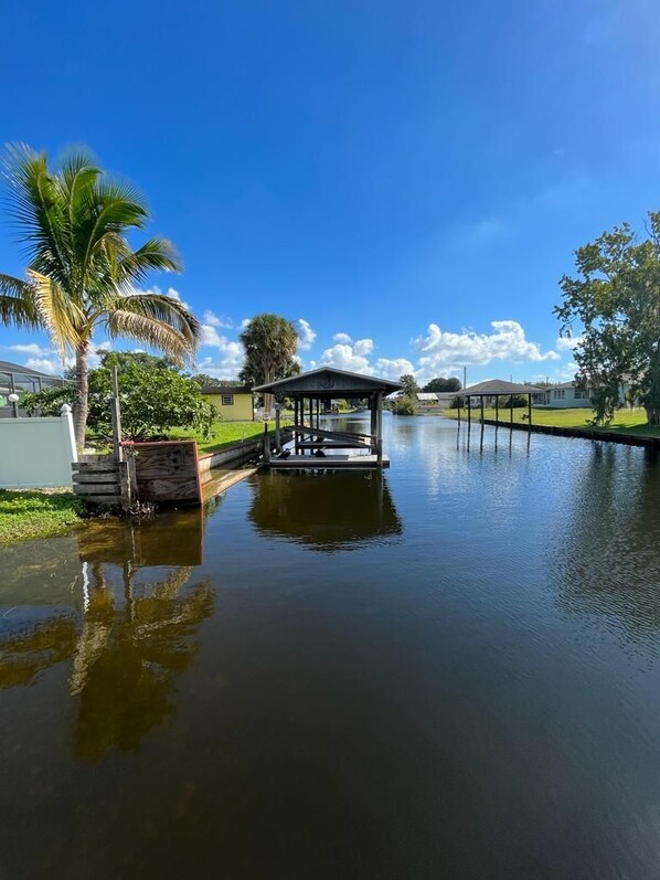 A calm water body with a dock and a covered structure, surrounded by greenery and clear skies.
