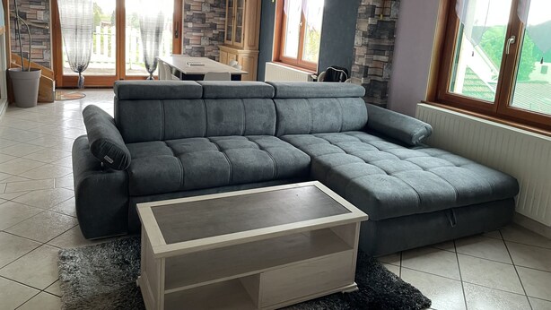 Ein modernes Wohnzimmer mit einem grauen Ecksofa, einem Holztisch und einer Wand mit Steinmuster.