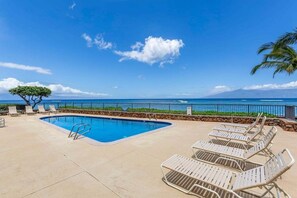 A pool area with lounge chairs and a view of the ocean.