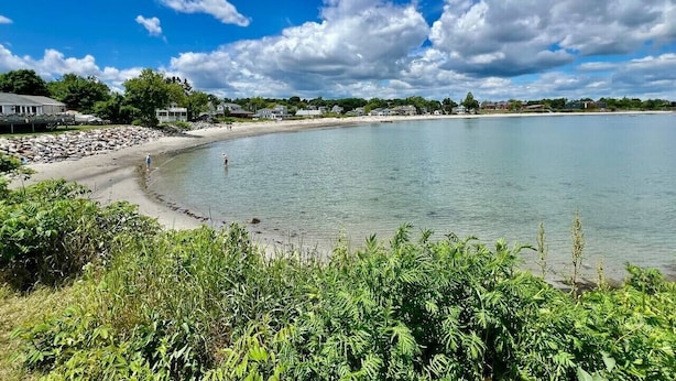 Un paisaje costero con cielo despejado, una playa arenosa y una masa de agua tranquila.