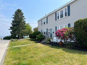 A two-story house with a front porch, a large tree, and a flower bed.