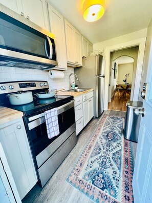 Une cuisine avec des meubles blancs, une cuisinière, un four à micro-ondes, un évier et un tapis à motifs.