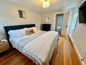 Une chambre à coucher comprenant un lit, une table de chevet, une commode et une porte donnant sur une autre pièce.