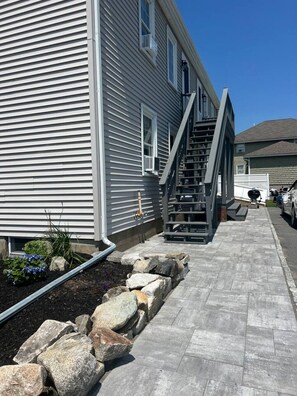 A residential building with a gray exterior, a stone retaining wall, and a paved walkway.