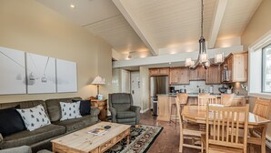 A spacious living area with a sofa, coffee table, and a dining table with chairs. There is a kitchen area with wooden cabinets and a refrigerator. - Ski-In/Ski-Out Condo with Sweeping Slopeside Views! (Steamboat Springs)