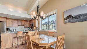 A modern kitchen with wooden cabinets, a central island, and a dining area with a large table and chairs. - Ski-In/Ski-Out Condo with Sweeping Slopeside Views! (Steamboat Springs)