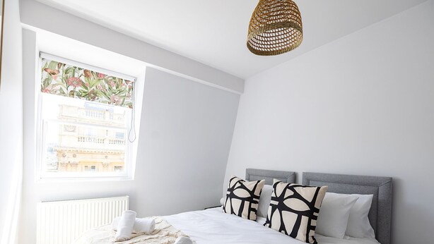A bedroom with a large bed, a window with a view of buildings, a radiator, and a woven light fixture. - Stunning apartment in central location - Pass the Keys (Bath)
