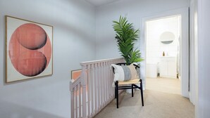 A hallway with a white railing, a chair with a striped cushion, a large potted plant, and a framed artwork on the wall. - Stunning apartment in central location - Pass the Keys (Bath)