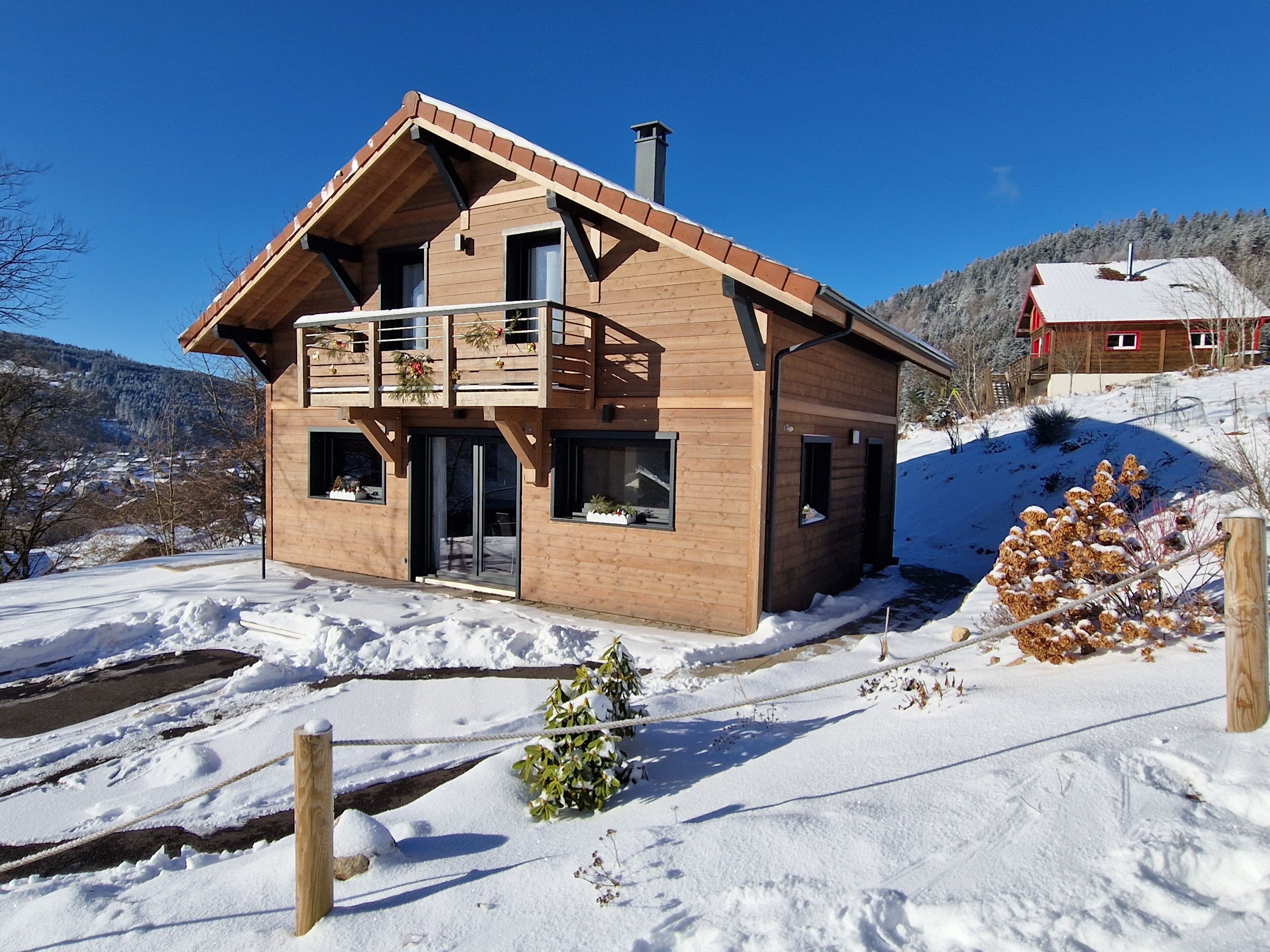 A wooden chalet with a balcony, a chimney, and a view of a snowy landscape.
