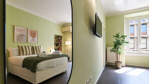A bedroom with a bed, bedside table, lamp, and a potted plant. - Sweett | Corso Como III (Milano)