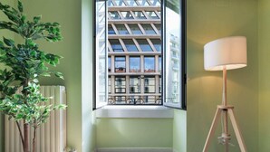A room with a large window, a potted plant, and a floor lamp. - Sweett | Corso Como III (Milano)