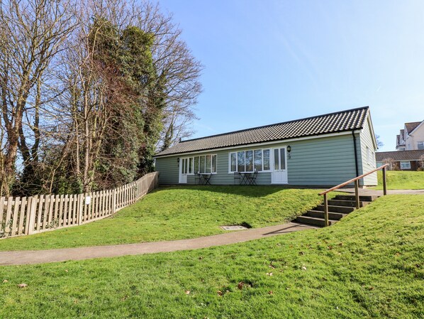 A single-story house with a tiled roof, a small front porch, and a staircase leading to the entrance. - 15 The Dell (Norwich)