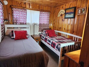 Une chambre dans un chalet en bois, avec deux lits, une petite table et un ventilateur.