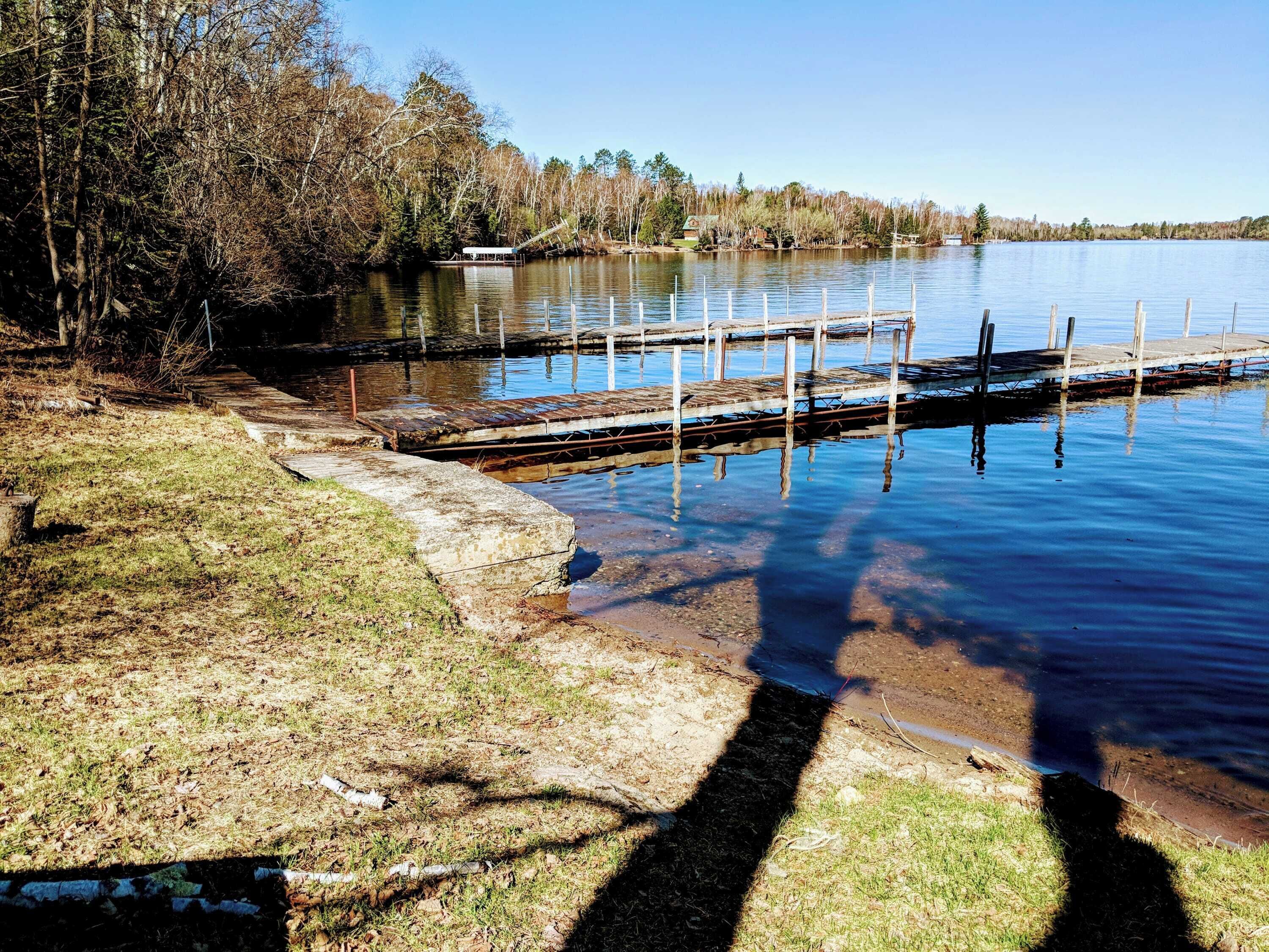 A lakeside dock with a grassy bank and trees in the background.