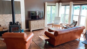 Una sala de estar acogedora con chimenea, sofás de cuero, televisor y grandes ventanales con vistas al exterior.