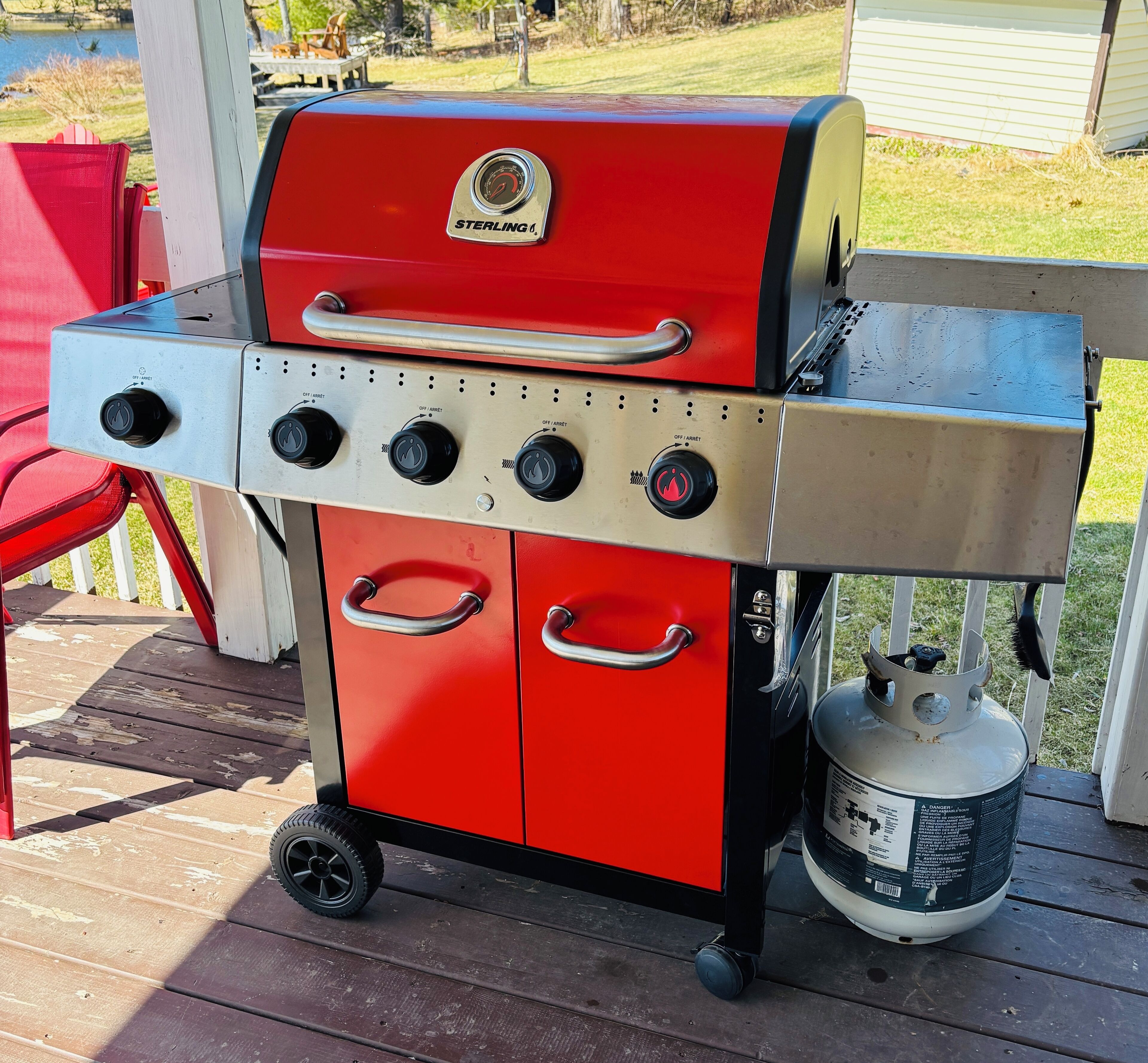 Un barbecue portatif rouge et argenté, doté de plusieurs brûleurs et d’une bouteille de propane.