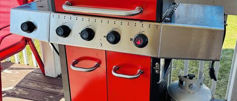 Un barbecue portatif rouge et argenté, doté de plusieurs brûleurs et d’une bouteille de propane.