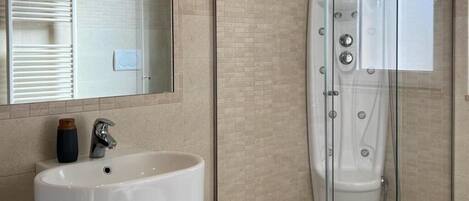 Un baño con un lavamanos blanco, un espejo y una ducha con mampara de vidrio.