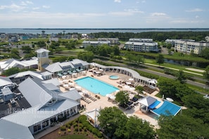 A residential area with a swimming pool surrounded by lounge chairs and umbrellas, a tennis court, and a view of the water. - 27587 S Nicklaus - beautiful home in The Peninsula ~ (Millsboro)