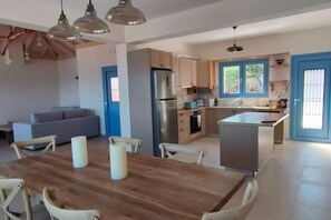 A modern kitchen with a central island, a dining area with a wooden table and chairs, and a living room with a sofa. - Augustela Villa Seaview Vacation Villa (Kefalonia)