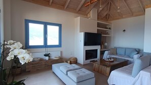 Ein geräumiges Wohnzimmer mit großem Fenster, Kamin, Fernseher und einer gemütlichen Sitzecke.