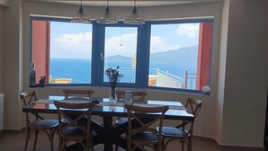 Ein Essbereich mit Tisch und Stühlen, einer Blumenvase und Blick auf das Meer durch große Fenster.