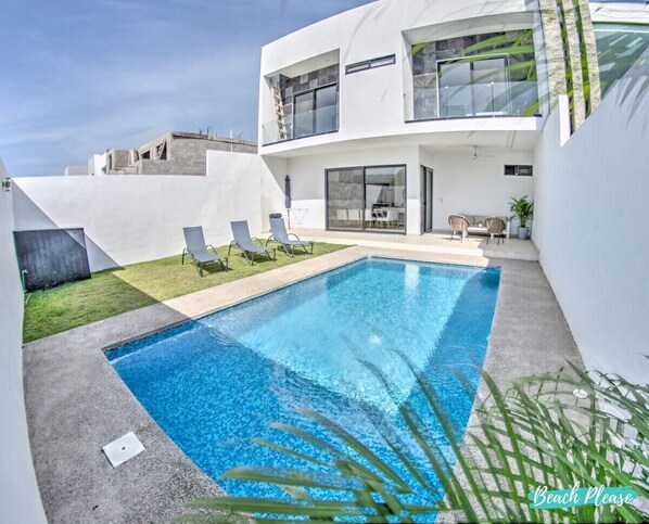 A modern pool area with a rectangular pool, lounge chairs, and a two-story building with large windows.