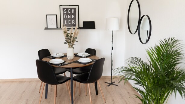 A dining area with a wooden table, black chairs, a vase with dried plants, and framed artwork on the wall. - Modern Stilvolle Fewo63qm 3 Zimmer (Hamm)
