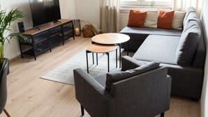 A modern living room with a grey sofa, a TV on a wooden stand, a small round table, and a potted plant. - Modern Stilvolle Fewo63qm 3 Zimmer (Hamm)