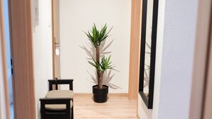 A narrow hallway with wooden flooring, a potted plant, a small table with chairs, and a mirror on the wall. - Modern Stilvolle Fewo63qm 3 Zimmer (Hamm)