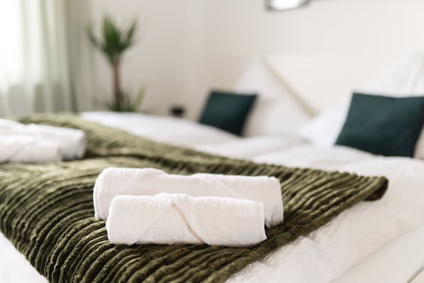A neatly made bed with a green textured blanket and white pillows, including a folded white towel.