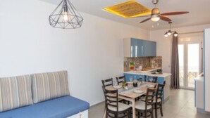 Una sala de estar moderna con un sofá azul, una mesa de comedor y sillas. Hay una zona de cocina con armarios azules y un ventilador de techo.