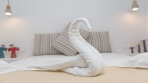 Una cama bien hecha con una manta blanca y almohadas, dos lámparas colgantes y una almohada a rayas en la cama.