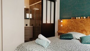Un dormitorio con cama, cabecera de madera, espejo, armario y baño con puerta de cristal.