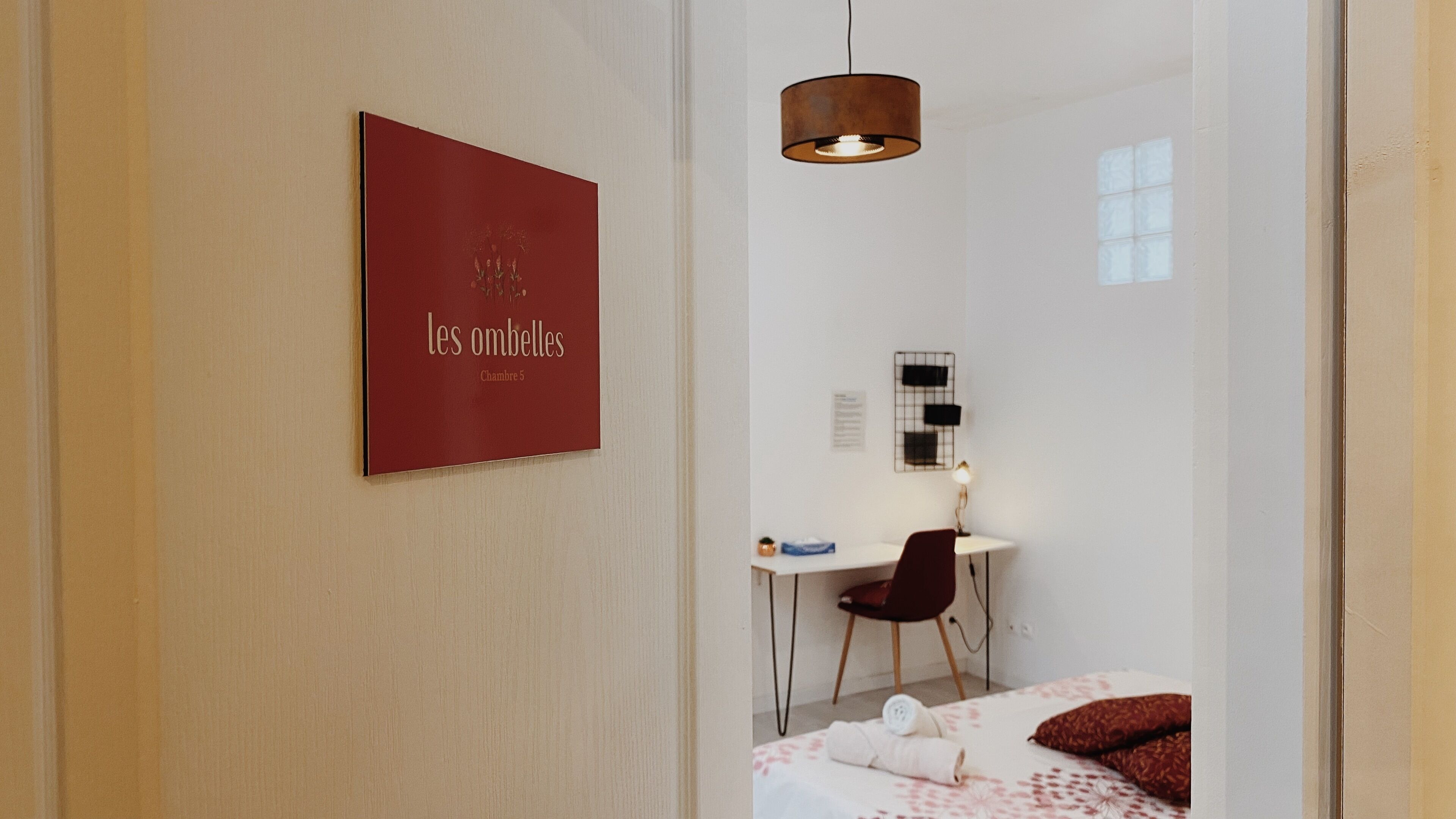 Habitación de hotel con cama, escritorio, silla, lámpara colgante y un cartel en la pared.