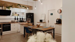 Una cocina moderna con armarios blancos, un refrigerador negro, una cafetera y un comedor con una mesa y sillas de madera.
