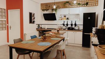 A modern kitchen with a dining area, featuring a wooden table, chairs, a refrigerator, and a coffee machine.