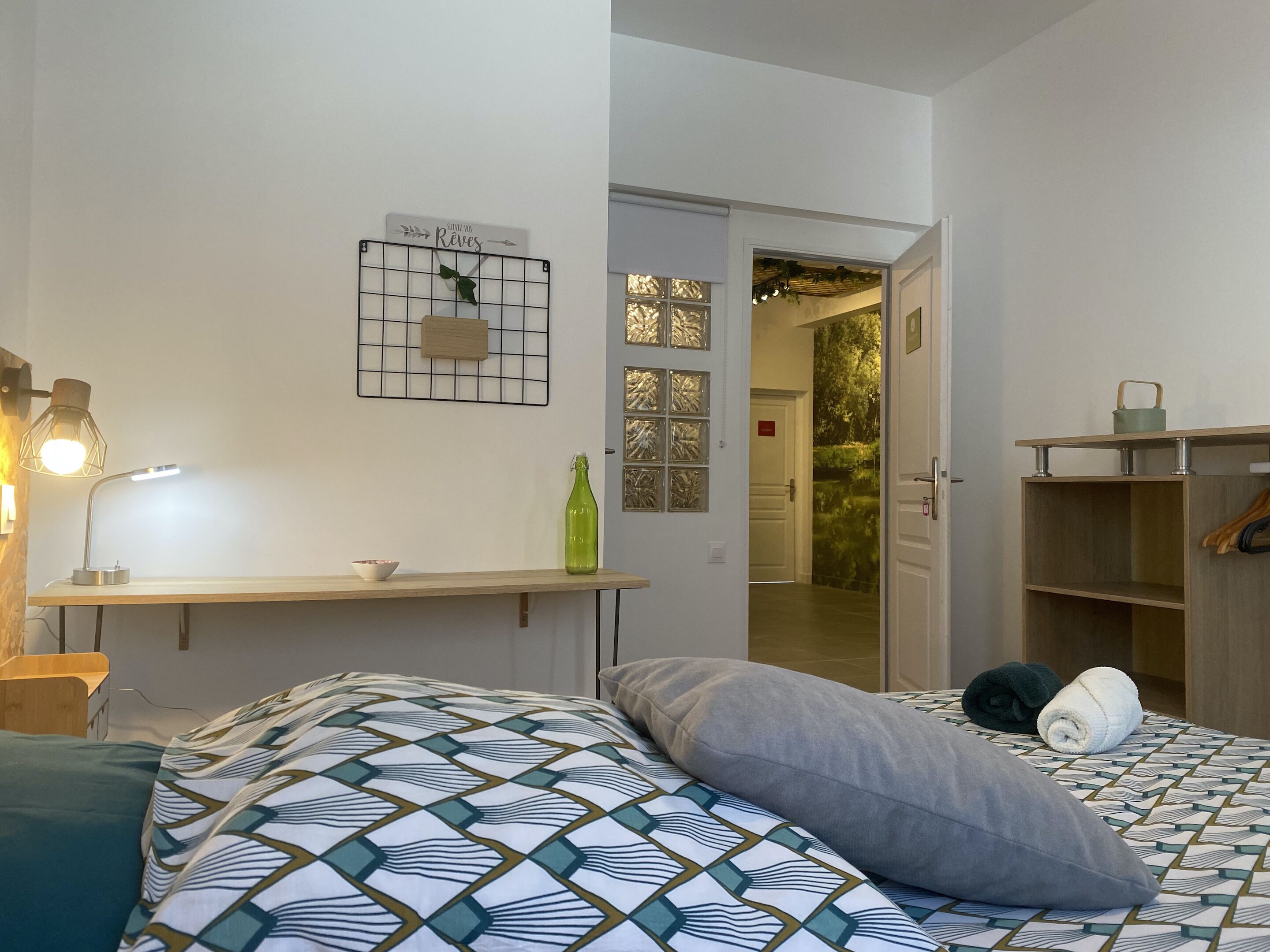 Ein Schlafzimmer mit einem Bett, einem Nachttisch, einer Lampe, einer grünen Flasche und einer Wanddekoration.