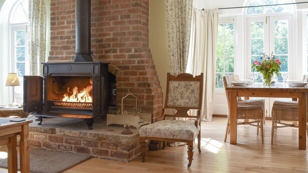 A cozy room with a brick fireplace, a dining table with chairs, and large windows with curtains.