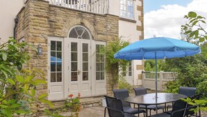 A stone building with a balcony, a round table with chairs, and a blue umbrella.