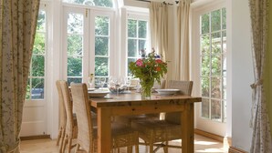 A dining area with a wooden table, wicker chairs, and a vase of flowers.