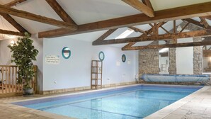 An indoor swimming pool with a tiled floor, wooden beams, a wooden bench, and a potted plant.