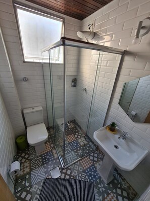 A bathroom with a glass shower enclosure, a toilet, a sink, and a patterned floor.