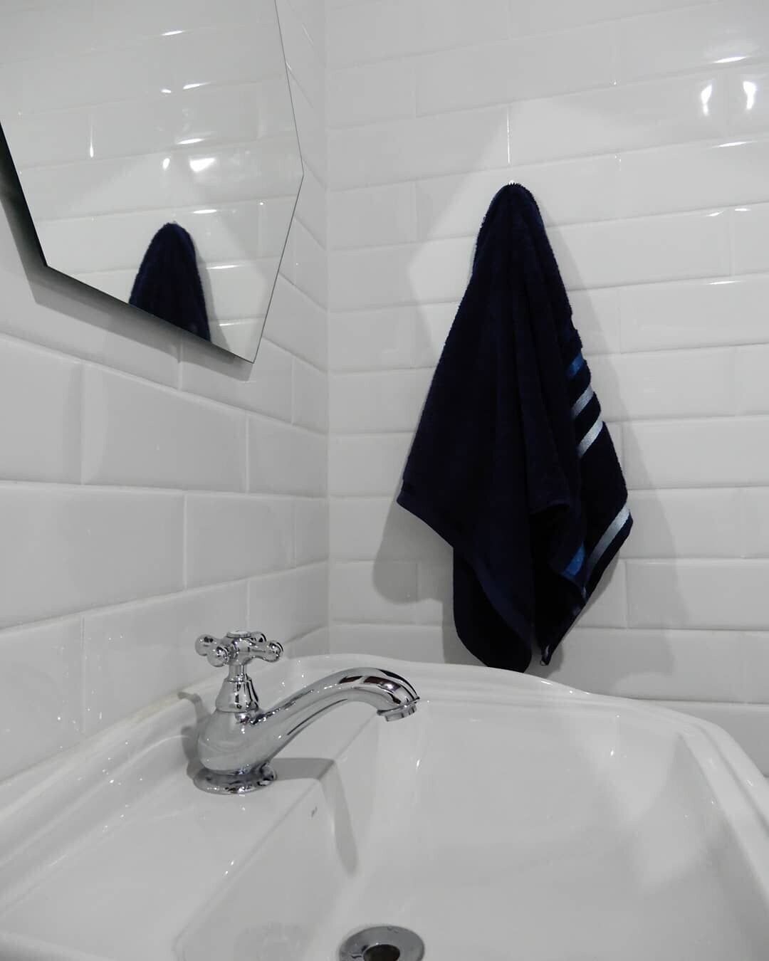 Un bagno con un lavandino bianco, uno specchio e un asciugamano appeso al muro.