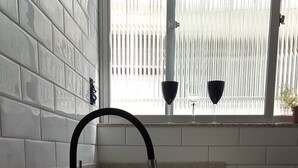A kitchen with a stainless steel sink, a black faucet, and a window with vertical blinds. - Apto na Pampulha próximo ao Mineirão  (Belo Horizonte)