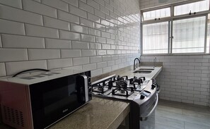 A kitchen with white subway tiles, a gas stove, a microwave, and a window with blinds.