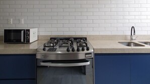 A kitchen with white subway tiles, a gas stove, a microwave, and a sink. - Apto na Pampulha próximo ao Mineirão  (Belo Horizonte)