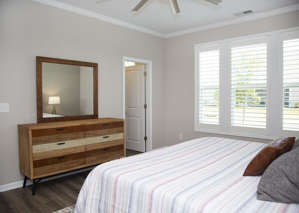 A bedroom with a wooden dresser, a bed with striped bedding, and a window with blinds.